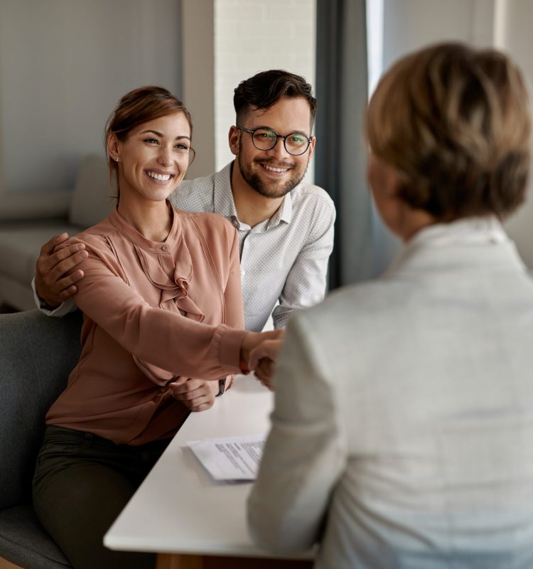 Young happy couple shaking hands with insurance agent during a meeting in the office.